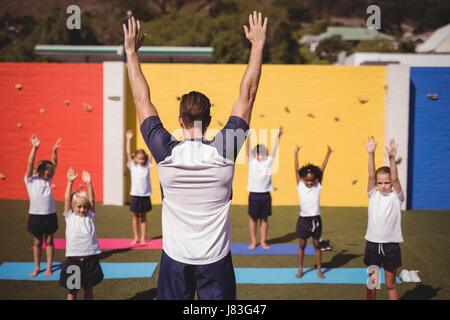 Coach teaching exercise to school kids in schoolyard