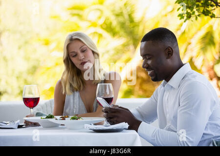 Young woman making face while man using phone at table in restaurant Stock Photo