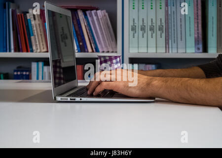 Guy or man or student or businessman working on a laptop computer in the library with the stacks of books around, photo from the side Stock Photo