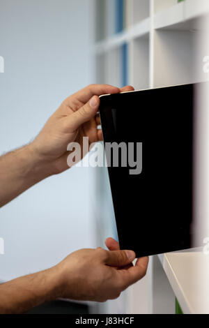 Guy or man or student or businessman taking a tablet with a blank screen from a bookshelf in the library with his hand Stock Photo