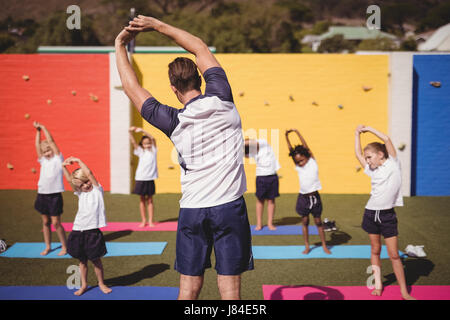 Coach teaching exercise to school kids in schoolyard