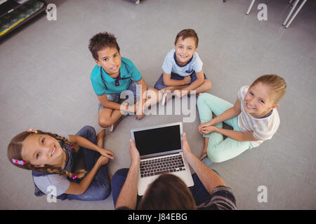 Overhead view of teacher and schoolkids using laptop in library at school Stock Photo