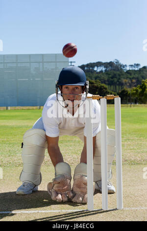 Wicketkeeper looking at ball crouching behind stumps on field against clear blue sky Stock Photo