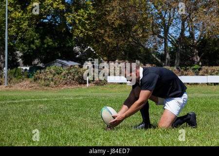 Side view of rugby player playing with ball on field against trees Stock Photo