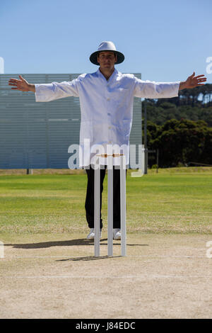 Full length of cricket umpire signalling wide ball during match against clear sky on sunny day Stock Photo