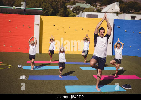 Coach teaching exercise to school kids in schoolyard Stock Photo