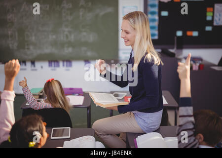 Schoolkids raising their hands while teacher teaching in classroom at school Stock Photo