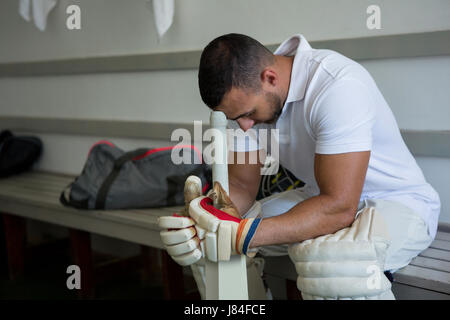 Close up of stressed cricket player sitting on bench at locker room