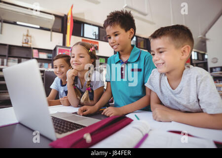 Happy schoolkids using laptop in library at school Stock Photo