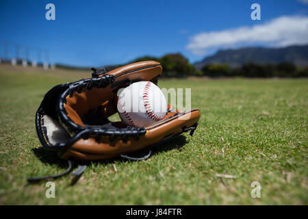 Close-up of baseball and glove on grassy field against sky Stock Photo