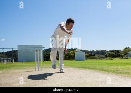 Bowler delivering ball during cricket match against clear blue sky on sunny day Stock Photo