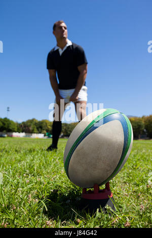 Close-up of rugby ball on grassy field with player standing in background Stock Photo