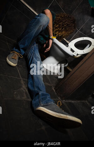 Man vomiting on toilet bowl in the washroom Stock Photo