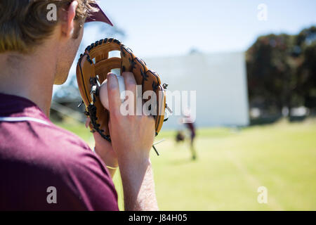 Baseball pitcher holding ball in glove at playing field on sunny day Stock Photo