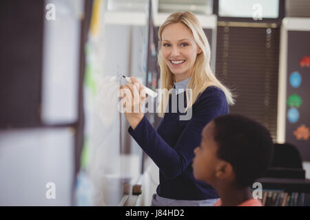 Portrait of teacher assisting schoolboy on whiteboard in classroom at school Stock Photo