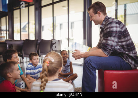 Happy teacher teaching schoolkids in library at school Stock Photo