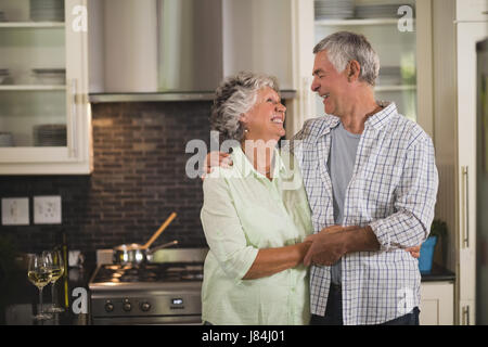 Cheerful senior couple embracing in kitchen at home Stock Photo