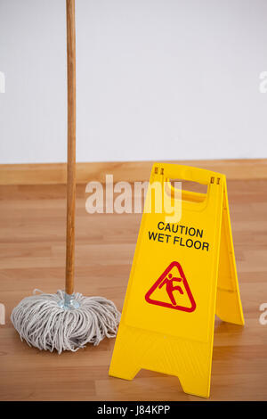 Mop with wet floor caution sign on wooden floor Stock Photo