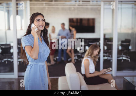 Young businesswoman talking on mobile phone with colleagues in background at creative office Stock Photo