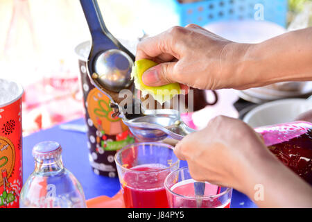 person squeeze green lemons on red sweet water Stock Photo