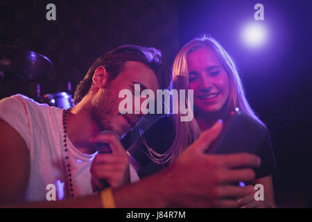 Young male and female musicians using mobile phone while practicing in nightclub Stock Photo