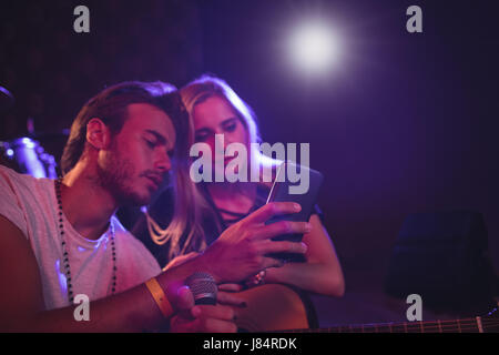 Male and female musicians using mobile phone while practicing in nightclub Stock Photo