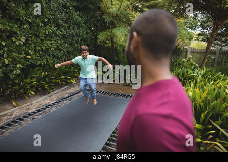 Side view of father looking at son jumping on trampoline Stock Photo