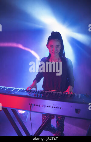 Portrait of smiling female musician playing piano in illuminated nightclub Stock Photo