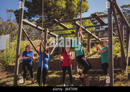 Female trainer instructing women to climb a rope in the boot camp on a sunny day Stock Photo