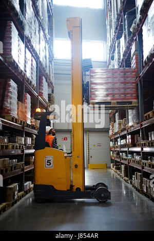 Loader lifting packed goods on shelf of storehouse Stock Photo
