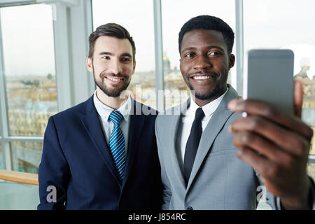 Portrait of handsome bearded businessman and his African partner taking smartphone selfie smiling to camera Stock Photo