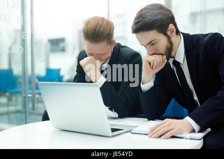 Stressed businessmen sitting by workplace in front of laptop Stock Photo