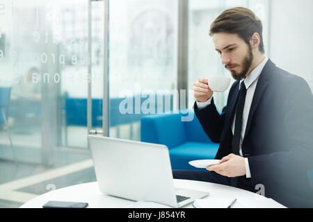 Businessman drinking tea and reading online news in office Stock Photo