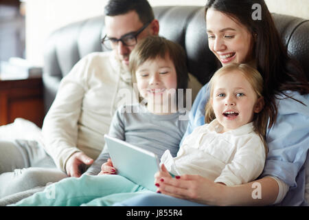 Happy family of four with touchpad sitting on sofa Stock Photo