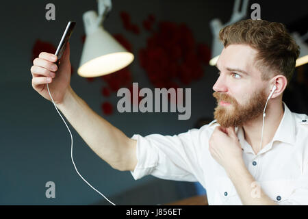 Side view portrait of handsome bearded man looking up at smartphone camera posing for selfie photo Stock Photo