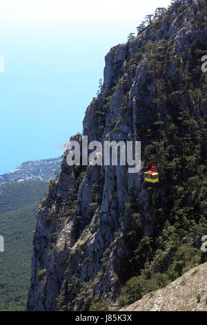 Yellow overhead cable car on background with very high mountain and sea Stock Photo