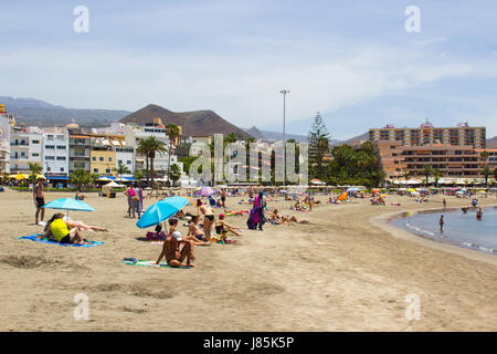 The sandy bay at Los Cristianos in Tenerife with holiday makers sun bathing with the ferry terminal and ships in the background Stock Photo