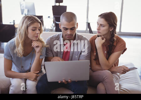 Serious young business colleagues working together over laptop while sitting at creative office Stock Photo