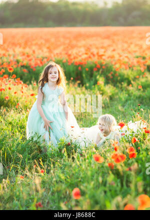 childhood, entertainment, weekends, celebration concept - two cheerful kiddies, wearing sunday outfits of blue and white colores, fooling around in the field of wild poppy flowers Stock Photo