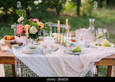 wedding, decoration, celebration, floral design, holidays concept - romantic table setting with white tablecloth, plates, crystal goblets, beautiful bouquet of roses and peonies and candels Stock Photo