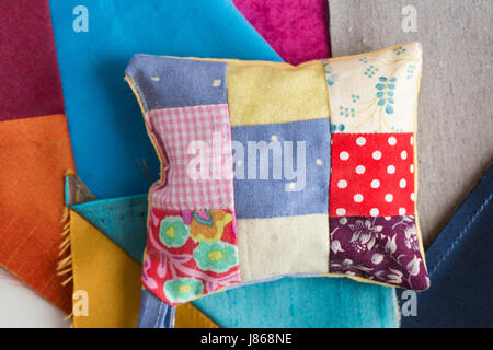 patchwork, quilting, sewing, tailoring and fashion concept - macro on pillow with background of blue, gray and sand flaps of fabric, closeup on beautiful colorful stitched cushion, flat lay, top view. Stock Photo