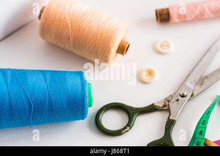 sewing tools, patchwork, tailoring and fashion concept - close-up on white desk in studio, colorful thread spools, measuring meter, buttons, many worked scissors, main equipment for needlework. Stock Photo