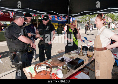 Lowestoft, UK. 24th May, 2017. Armed police officers, on patrol in Lowestoft town centre, take an interest in some wartime memorabilia including a fake incendiary device at a 1940s wartime stall. They chat with Ian Pycroft who, dressed as an air raid warden, was hosting one of the attractions at the Lowestoft 1940s Festival Weekend over the busy Spring Bank Holiday weekend in the UK. © Adrian Buck / Alamy Live News. Stock Photo