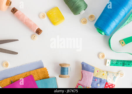 patchwork, sewing tools, tailoring and fashion concept - close-up on white desk with colorful skeins of thread, measuring meter, buttons, scissors, pincushion, equipment for needlework. Stock Photo
