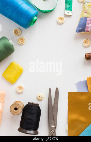 closeup sewing tools, patchwork, tailoring and fashion concept - tools on white table, colorful thread spools, buttons, meter, pincushion, scissors, pieces of colored patchwork fabric, soap, vertical. Stock Photo