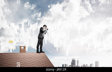 Businessman standing on roof and looking in binoculars. Mixed me Stock Photo