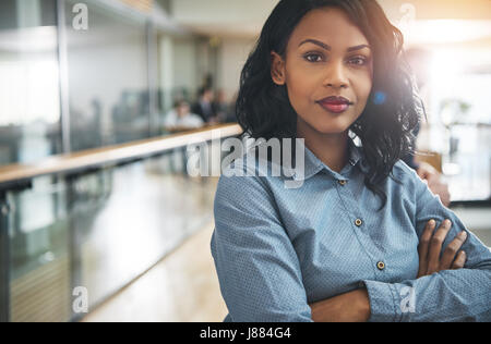 Pretty young dreamy African-American office worker standing with arms crossed and looking at camera. Stock Photo