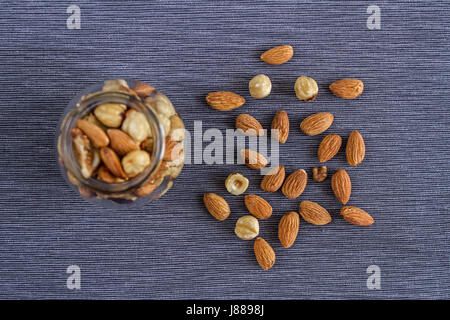 Appetizing nuts of walnuts, almonds and hazelnuts in a glass beautiful vase and on a gray textile background for a healthy snack. Stock Photo