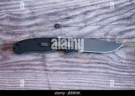 Black knife and gray wood background. Pocket knife in unfolded form with a pocket clip. Black knife. Stock Photo