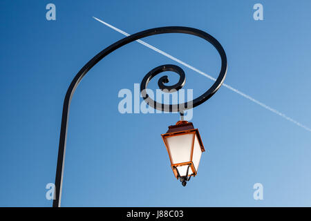 Shining Backlit Streetlamp and Airplane Trail in Background, Megeve, France Stock Photo